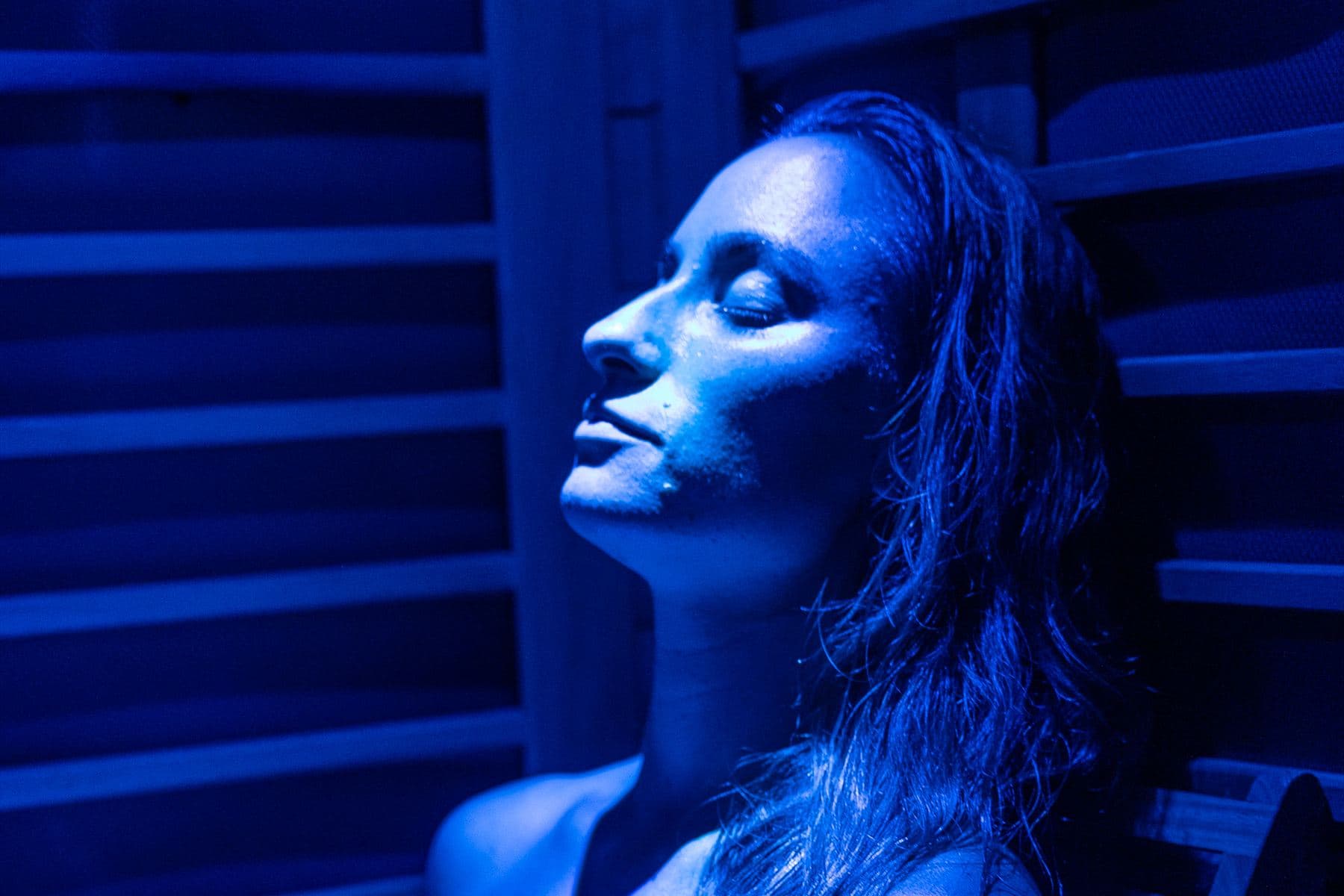 Close-up of a woman resting her head back in the infrared sauna, lit in blue