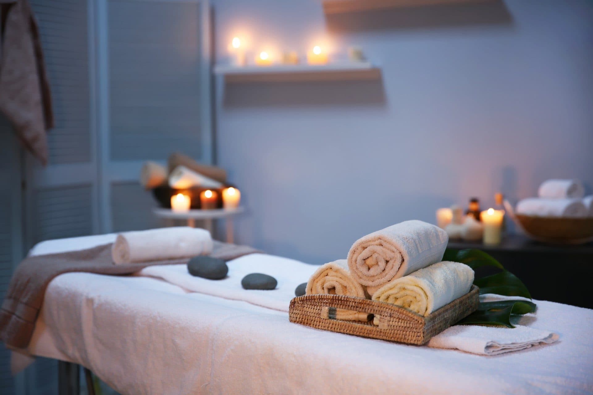 Candlelit massage room with rolled towels and hot stones